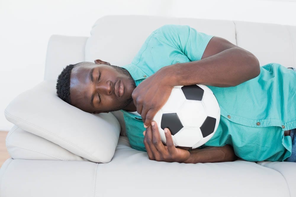 Football fan sleeping on couch hugging ball