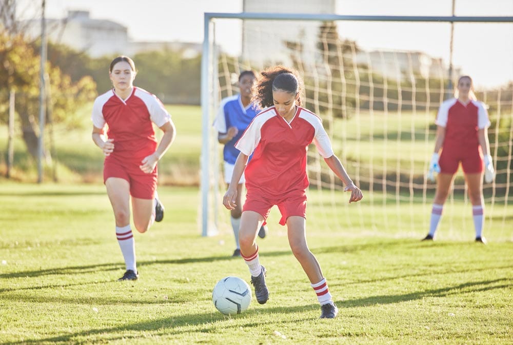Female football, sports and girls team playing match on field while kicking, tackling and running with a ball. Energy, fast and skilled soccer players in a competitive game against opponents