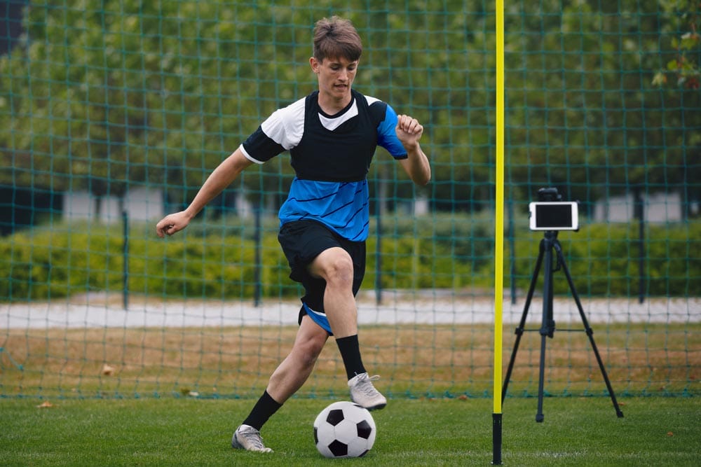 Young Football Soccer Player on Training With New Technology. New Technology in Soccer Training. Sports Athlete Running Ball. Tablet Device in the Background. Technology in today's Football