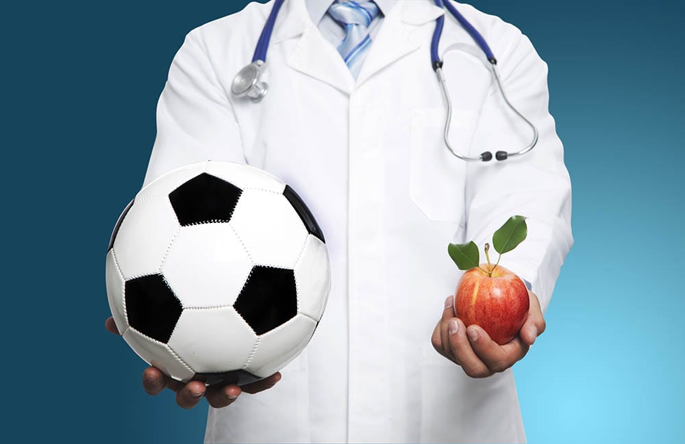 Doctor with black and white soccer ball and apple isolated on blue background