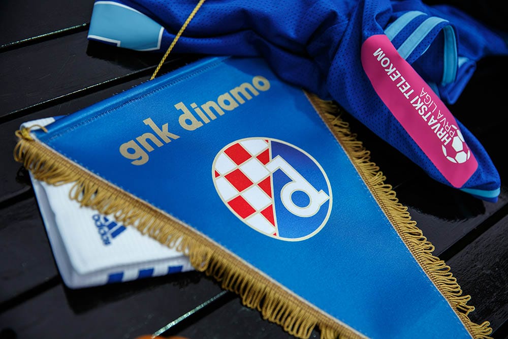 Emblem of GNK Dinamo on pennant, football club from Zagreb. T-Hrvatski Telekom Prva Liga logo on blue t-shirt. Adidas white captain's armband.