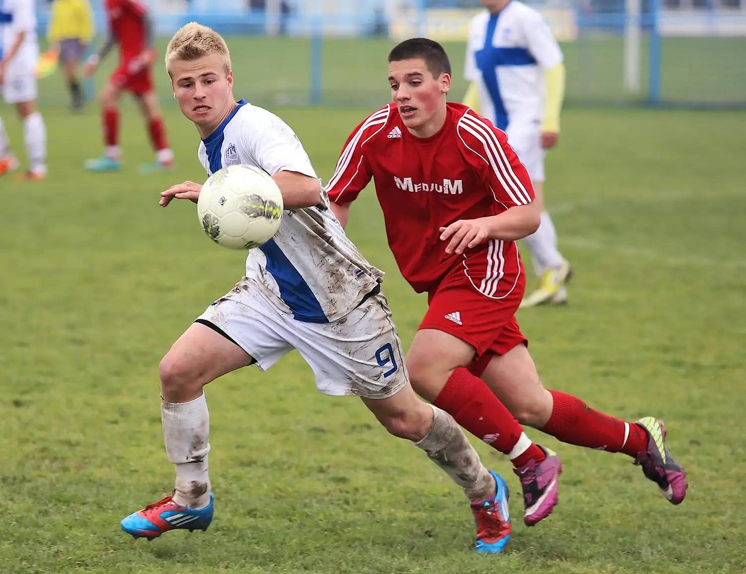 two football players competing for the ball. One is wearing white and blue, the other is in a red football kit