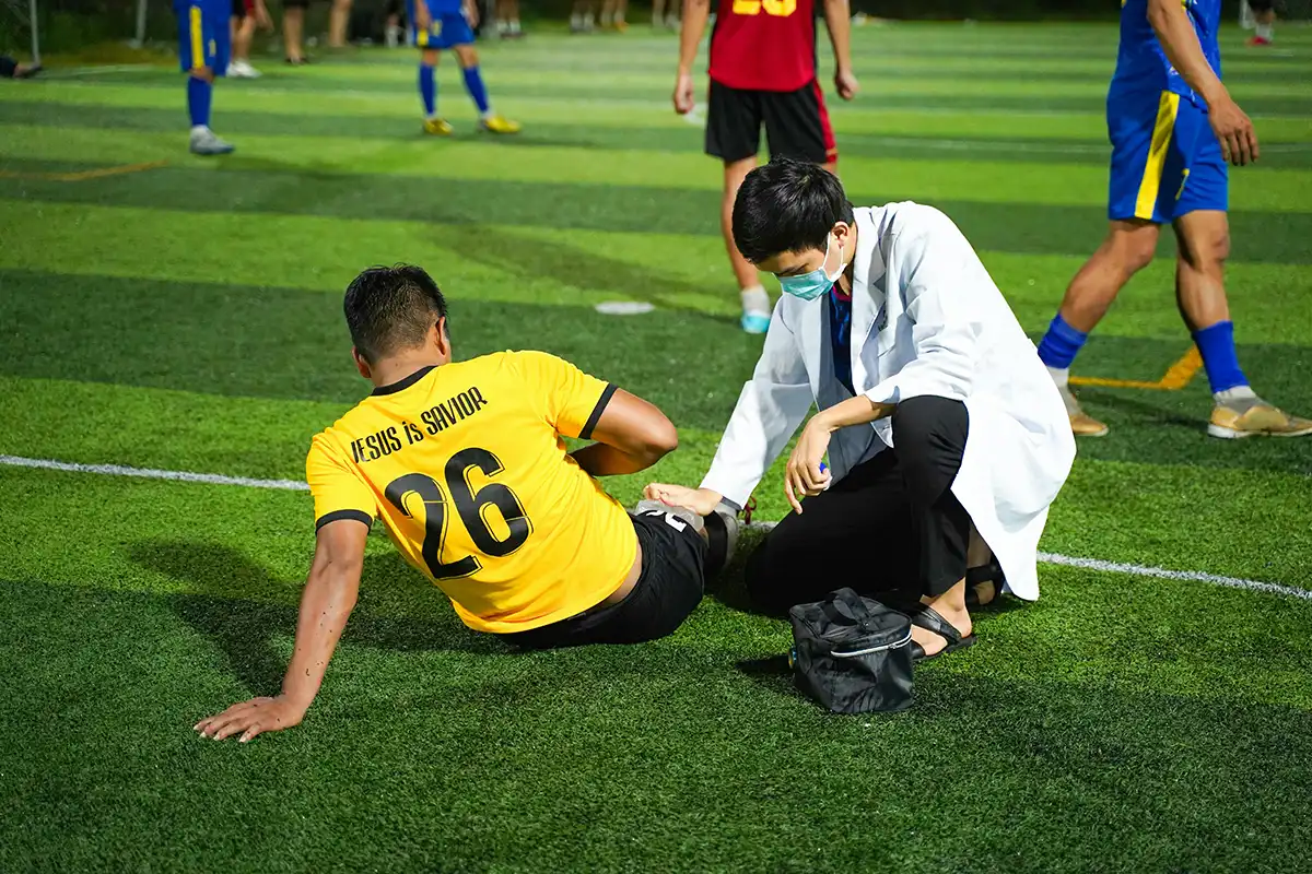 a football sat down on grass being attended to by a doctor with a mask on