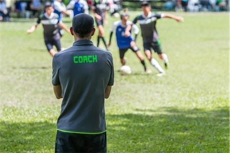 a man watching a football match wearing a t-shirt with the word coach on it