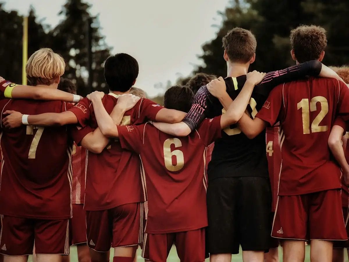 5 young footballers facing away from the camera wearing red kits with arms over the shoulders of each other