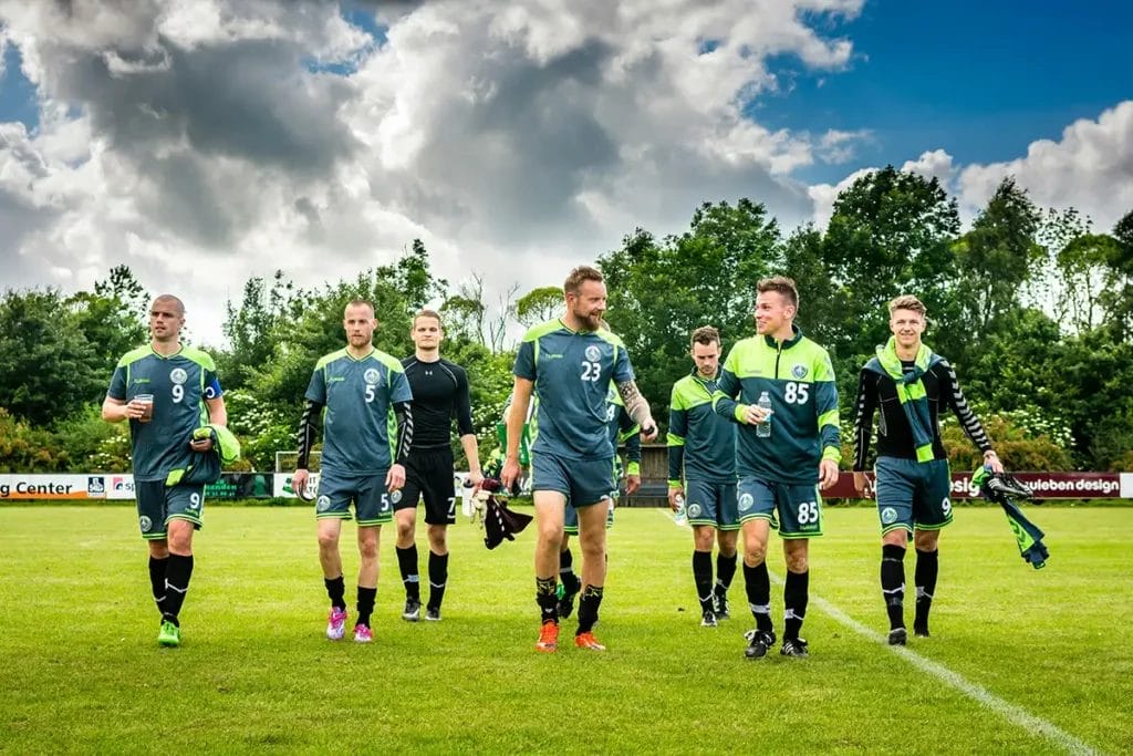 a group of male footballers leaving a football pitch after a game.